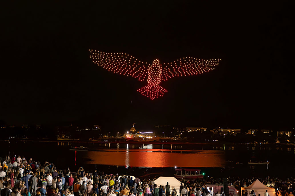 A large red and yellow bird made of drones over water (Drone Show Example)